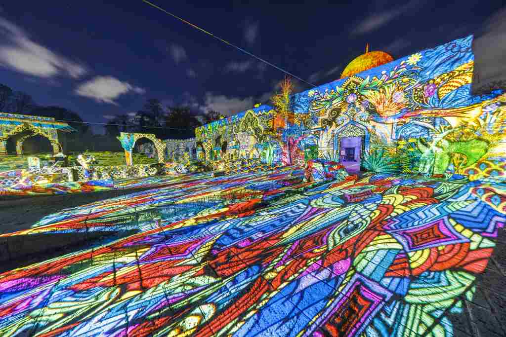 Bunte Lichtprojektionen bedecken nachts die Wände und den Boden eines Gebäudes im Freien.